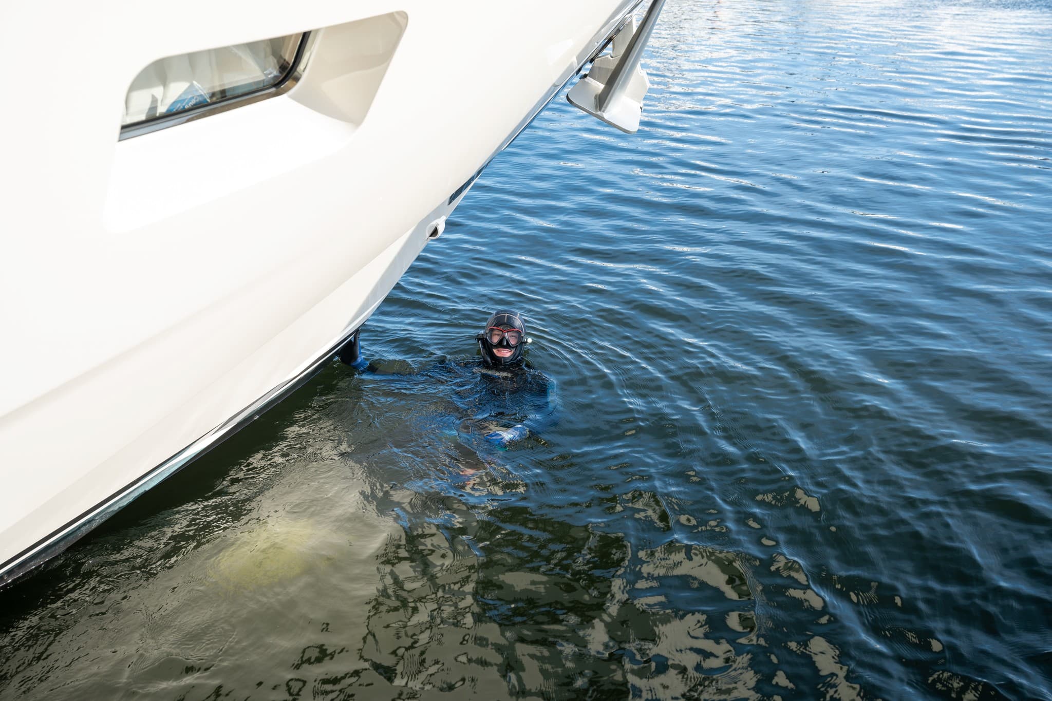 Diver in the water alongside a yacht hull at the dock