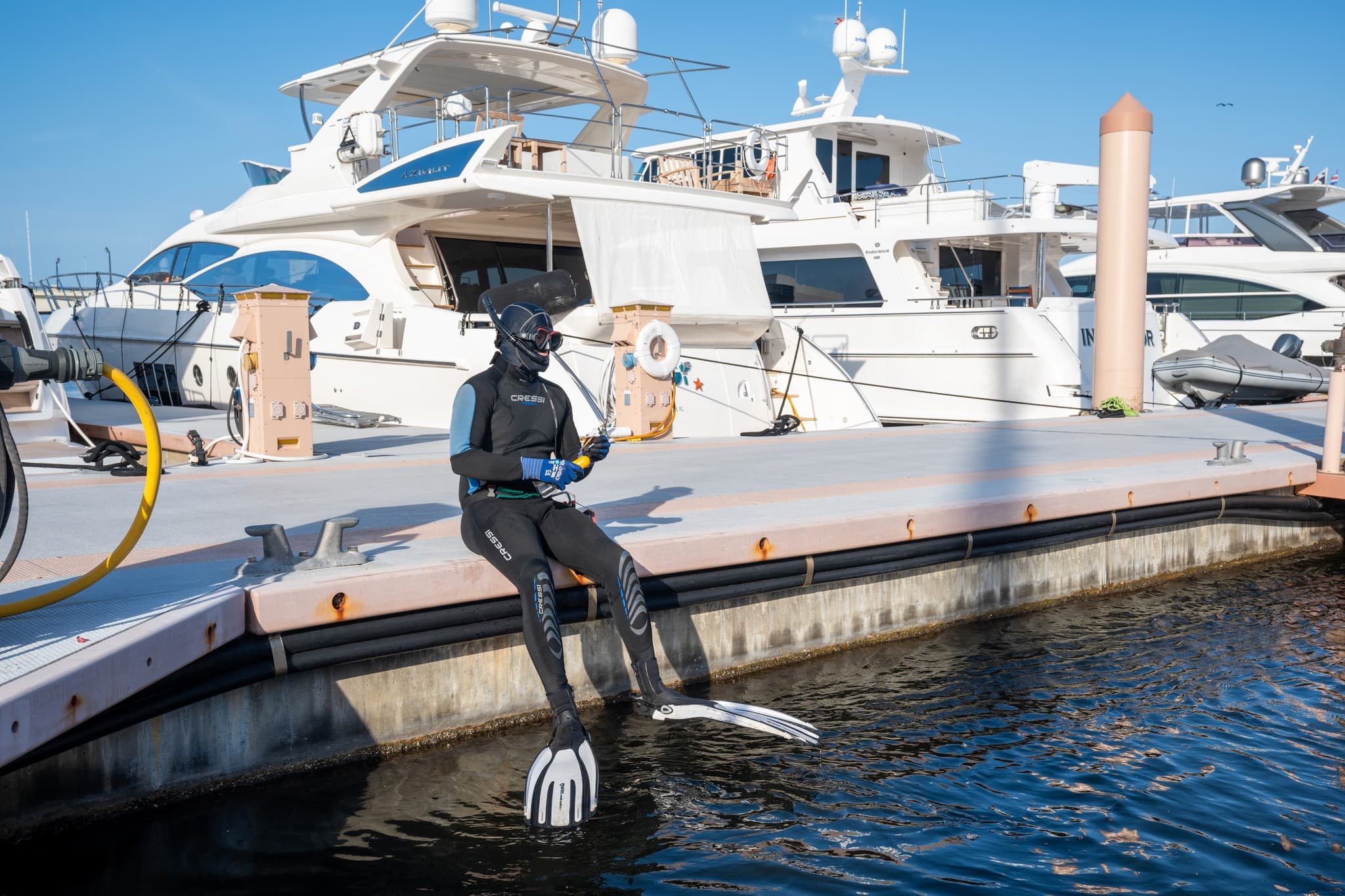 Diver seated on the dock edge with fins on, yachts behind