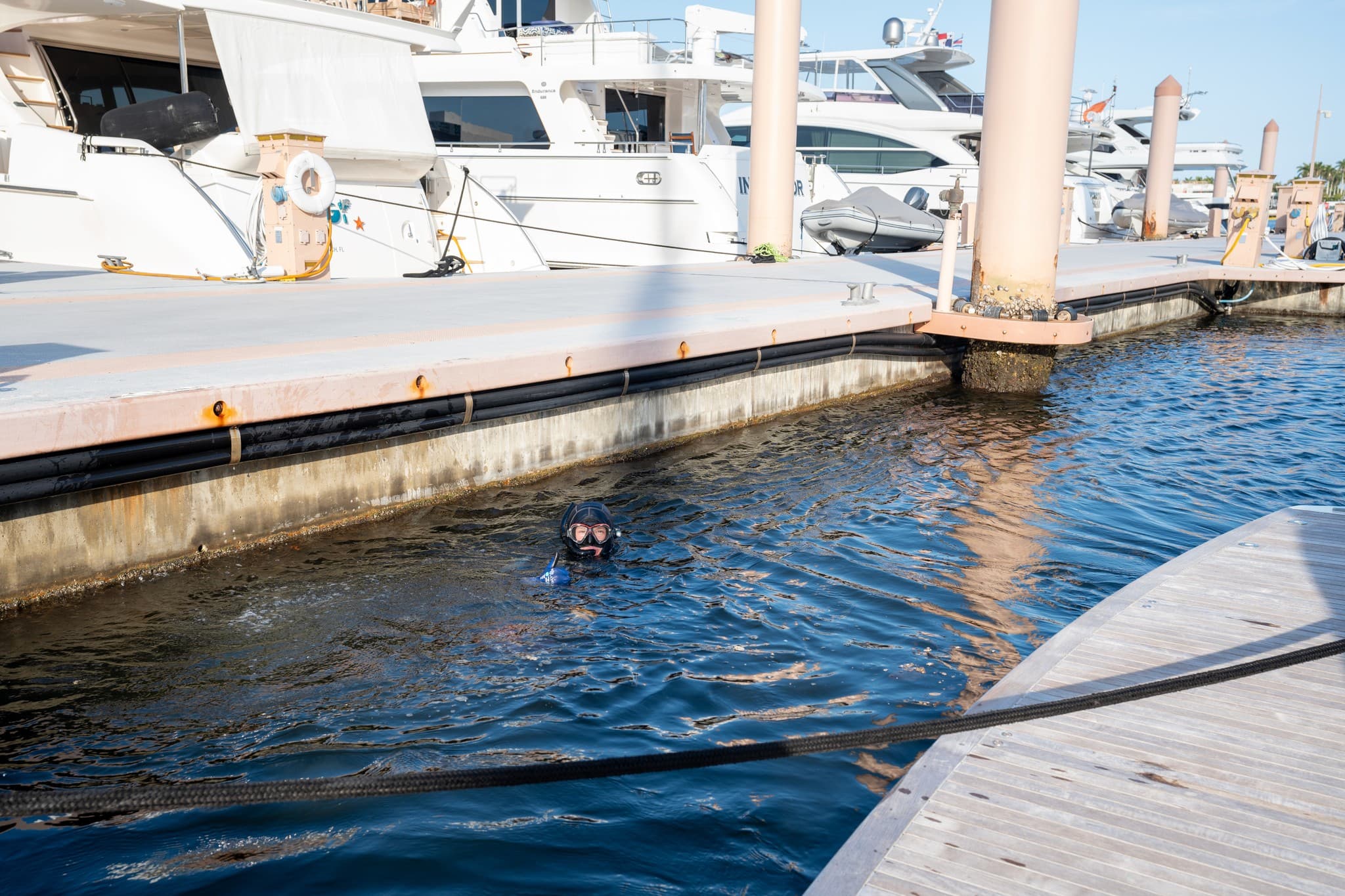 Diver swimming between marina docks toward a yacht