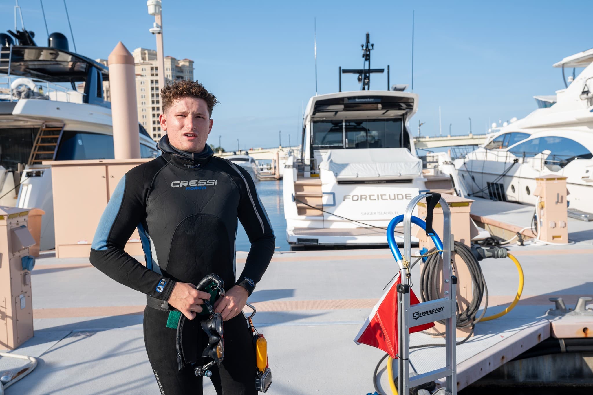 Diver in a wetsuit holding a hose on the dock